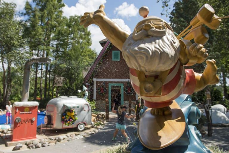 Santa Claus in swim trunks greets guests by a festive house and trailer, with snowy fun at Winter Summerland Miniature Golf.
