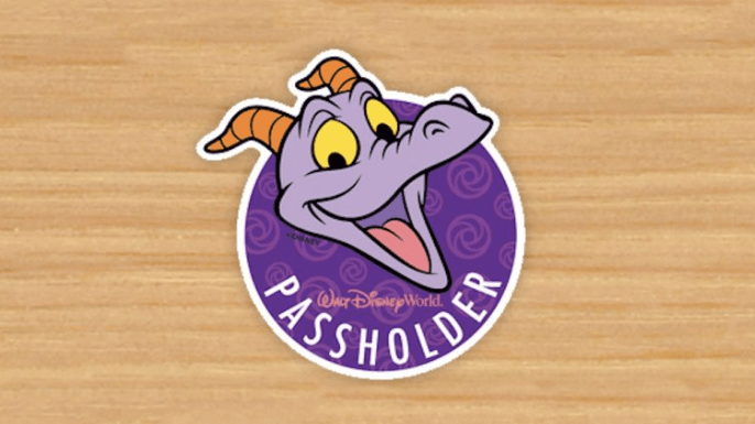 Figment’s smiling face on a purple Walt Disney World Annual Passholder sticker, set against a wooden surface.