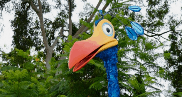 Kevin from UP sculpture with bright blue feathers and a big orange beak, set amid lush greenery at Disney’s Animal Kingdom.