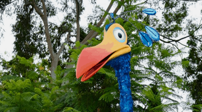 Kevin from UP sculpture with bright blue feathers and a big orange beak, set amid lush greenery at Disney’s Animal Kingdom.