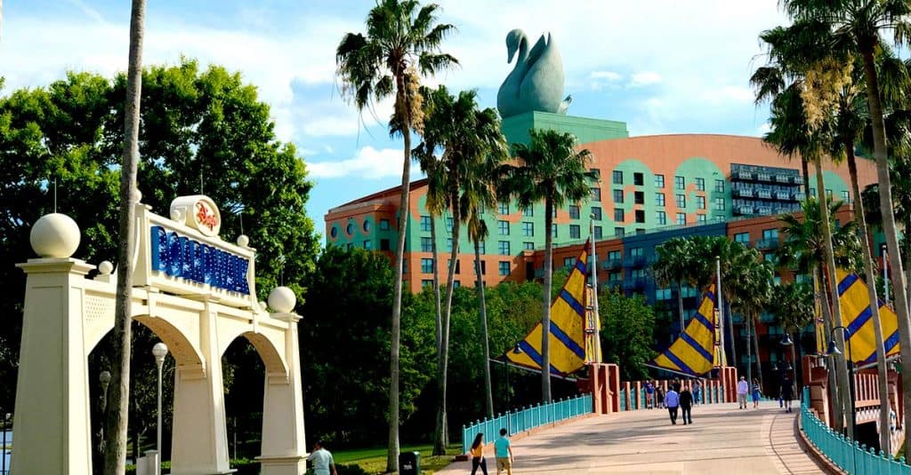 Walt Disney World Dolphin Hotel entrance at the Swan and Dolphin Resort with iconic swan statue, palm trees, and guests on the bridge.