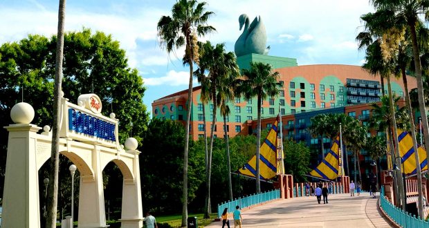 Walt Disney World Dolphin Hotel entrance at the Swan and Dolphin Resort with iconic swan statue, palm trees, and guests on the bridge.