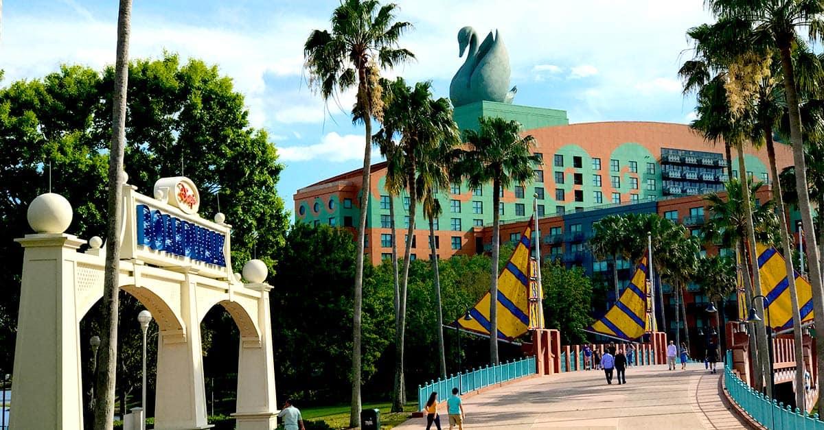 Walt Disney World Dolphin Hotel entrance at the Swan and Dolphin Resort with iconic swan statue, palm trees, and guests on the bridge.