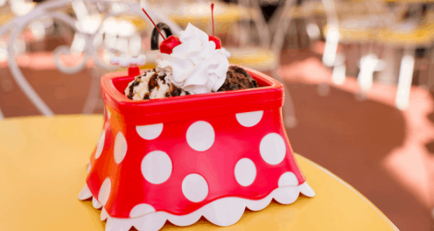 Minnie Mouse polka-dot bowl piled with ice cream, whipped cream, and cherries on a yellow table at Disney World’s celebration.