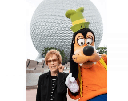 Goofy greets a smiling guest in front of Epcot’s iconic Spaceship Earth at Walt Disney World.
