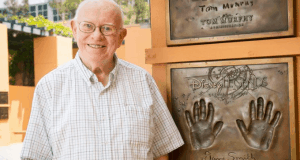 A cheerful Disney Legend stands beside their handprints and name on the iconic Walk, celebrating Disney’s legacy and stars like Dave Smith.