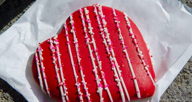 Heart-shaped red cookie with white icing and festive sprinkles, ready to delight guests at Disneyland’s Valentine event.