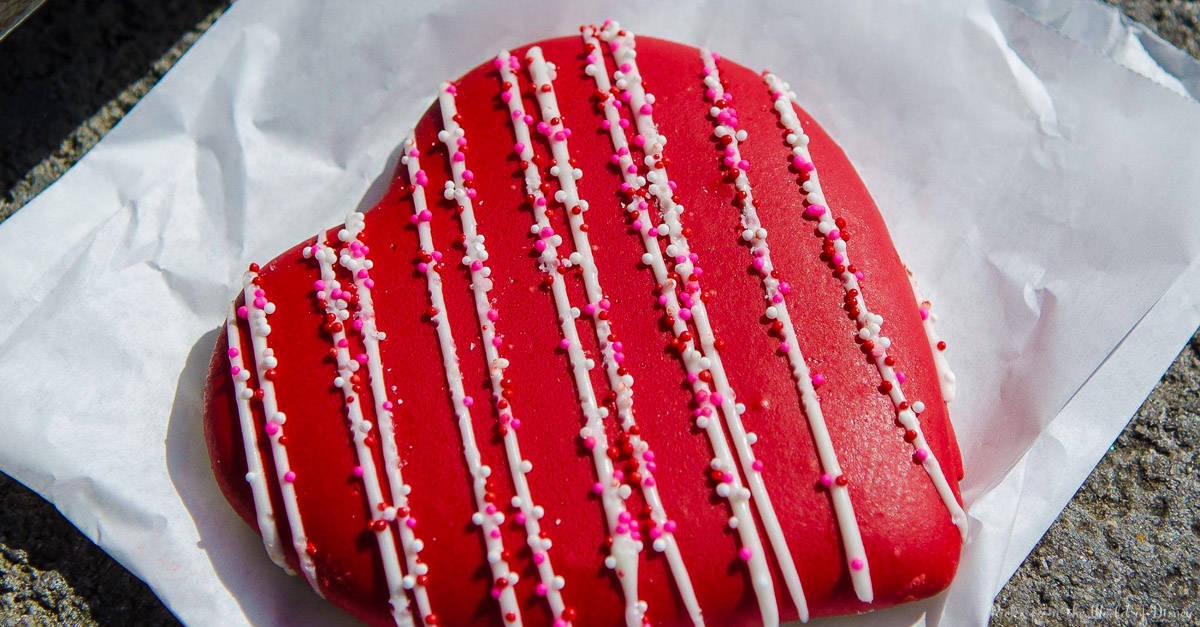 Heart-shaped red cookie with white icing and festive sprinkles, ready to delight guests at Disneyland’s Valentine event.