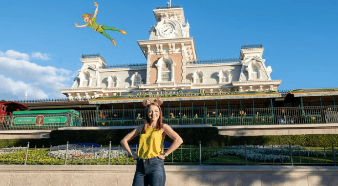 A guest beams at the Magic Kingdom entrance as Peter Pan flies overhead in a whimsical Disney PhotoPass Magic Shot experience.