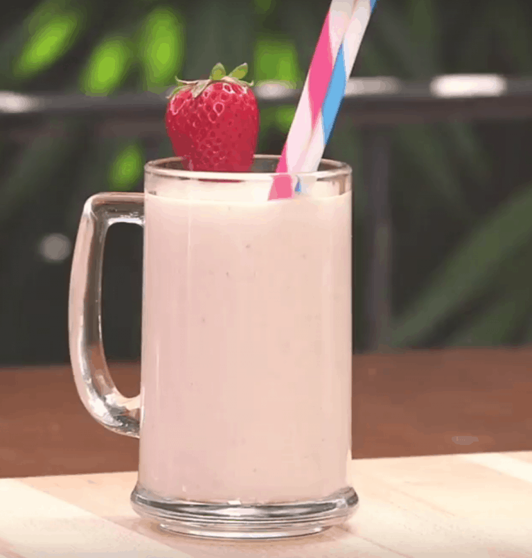 Strawberry milkshake with two straws and a fresh strawberry, served Disney World-style on the table.