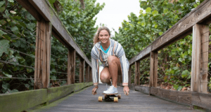 A guest skateboards along the scenic wooden walkway at Disney Springs, greenery all around and a big smile for the camera.