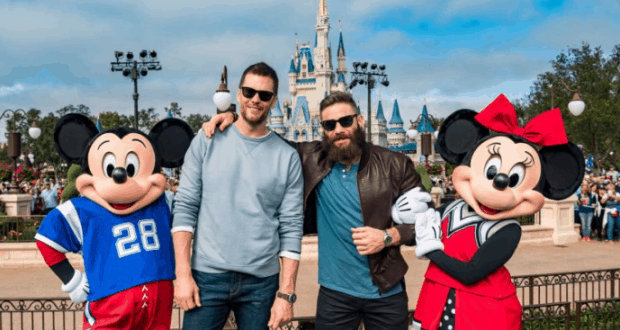 Patriots fans celebrate with Mickey and Minnie Mouse in front of Cinderella Castle at Walt Disney World on a sunny day.