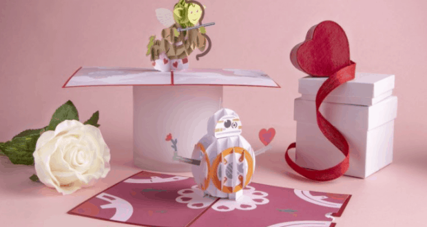 Valentine pop-up cards of a flower, droid, and cupid at Disney Springs, with a white rose and gift box on pink background.