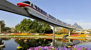 The Disney World monorail soars over vibrant gardens and a sparkling pond, capturing the magic of the park on a sunny day.