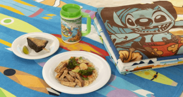 Splash Pack Bundle with Disney-themed food, dessert, cup, and Stitch towel on a colorful blanket at Walt Disney World water park.