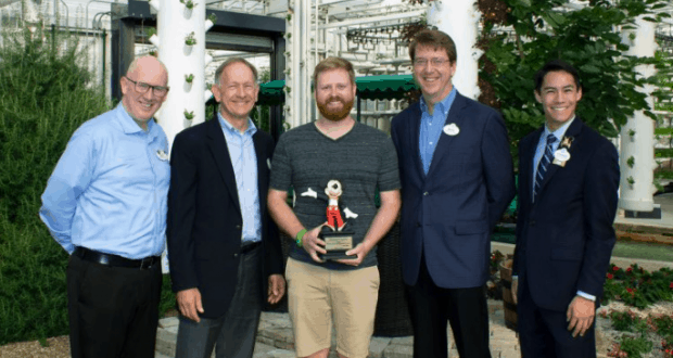 Five friends smile in a Disney World greenhouse, one proudly holding a Mickey Mouse trophy after the Behind the Seeds Tour.