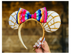 Golden headband with white and gold ears inspired by conchas, topped with a vibrant striped bow, perfect for Disney Parks fans.