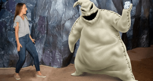 A guest appears surprised as Mickey Mouse, holding oversized dice, greets her inside a magical Disney World cave-themed photo spot.