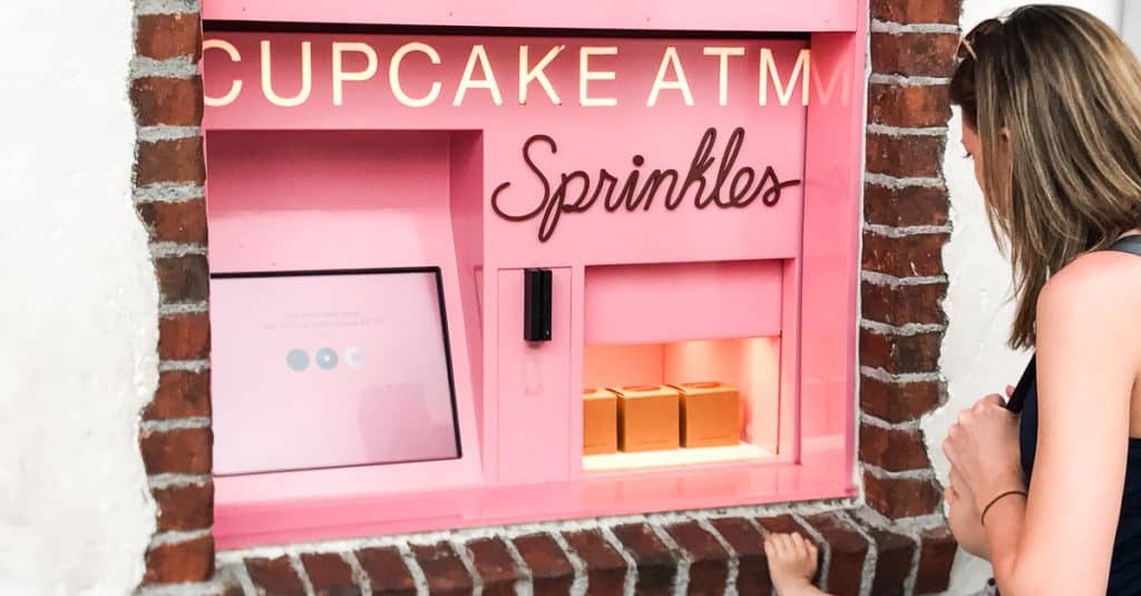 A guest grabs treats from the bright pink Sprinkles cupcake ATM outside Disney World, ready for a sweet theme park pick-me-up.