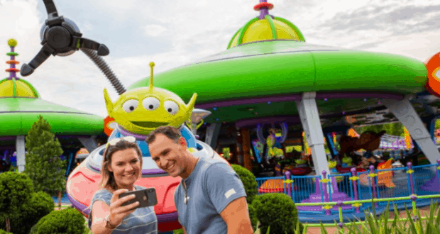 Happy couple snaps a selfie by Toy Story Land’s green alien ride, celebrating their 1st anniversary at Walt Disney World.