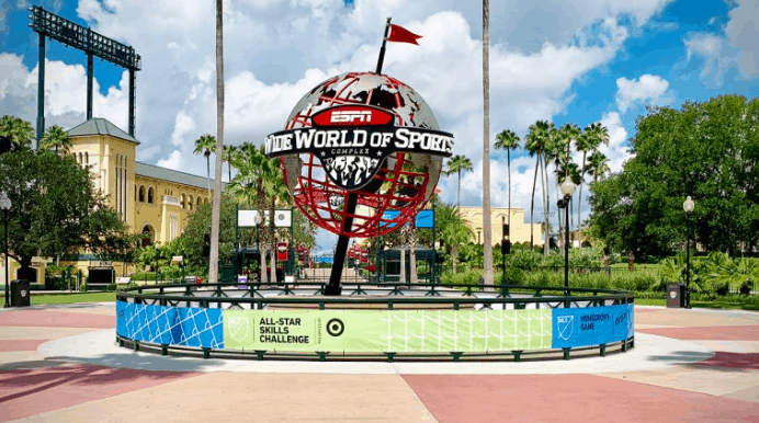 Iconic red globe at ESPN Wide World of Sports, framed by palms and banners, spotlights Disney’s All-Star sports excitement.
