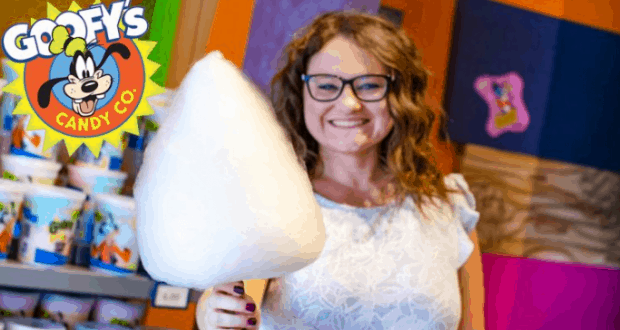 Guest enjoying fluffy cotton candy at Goofy's Candy Co., surrounded by vibrant Disney World decor and magical atmosphere.