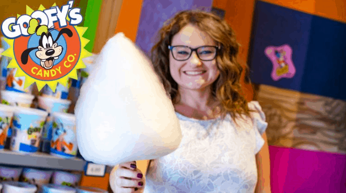 Guest enjoying fluffy cotton candy at Goofy's Candy Co., surrounded by vibrant Disney World decor and magical atmosphere.
