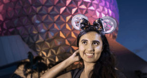 Disney fan beams in a glowing light-up headband and Mickey ears before the dazzling night-lit geodesic dome at Walt Disney World.