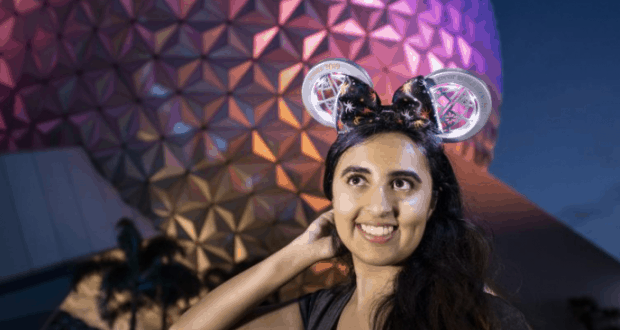 Disney fan beams in a glowing light-up headband and Mickey ears before the dazzling night-lit geodesic dome at Walt Disney World.