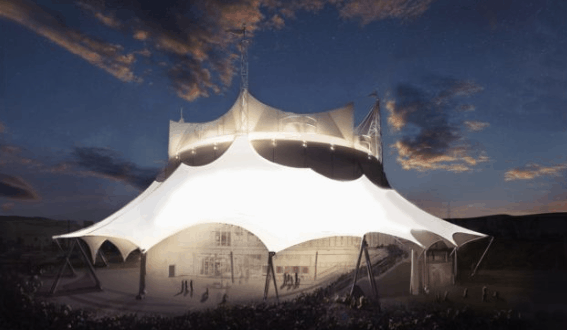 The glowing Cirque du Soleil white tent lights up Disney Springs at night as guests gather beneath a dramatic evening sky.