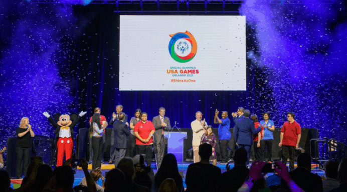 Mickey Mouse joins athletes on stage at Disney World for the 2022 Special Olympics USA Games, with confetti filling the air.
