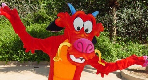 A bright red dragon with blue horns playfully entertains guests outdoors, channeling the energy of Disney World performers.