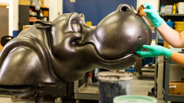 A guest offers a treat to a lifelike hippo sculpture in a whimsical workshop, echoing the magic of Disney's Riviera Resort.