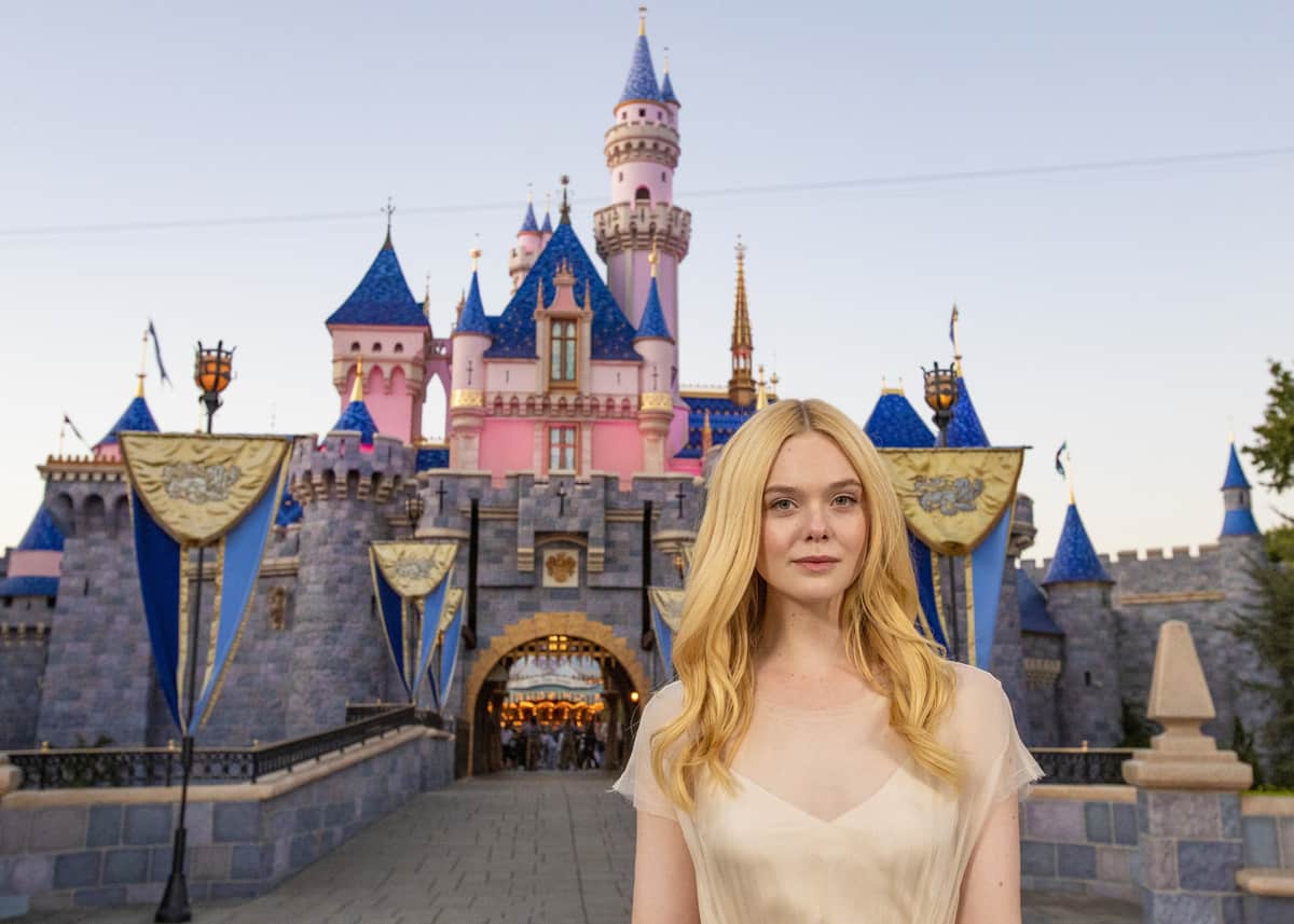 Disneyland guest with flowing blonde hair poses before Sleeping Beauty Castle, embodying Elle Fanning's Maleficent flair.