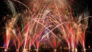 Dazzling fireworks explode over Epcot’s skyline, their colors mirrored on the lagoon, celebrating Epcot Forever at Disney World.