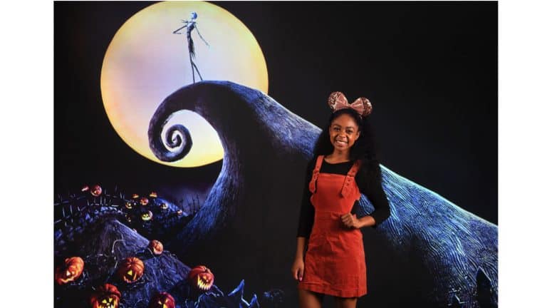 Capture Halloween memories at Disney Springs with a guest in mouse ears before the iconic Nightmare Before Christmas backdrop.