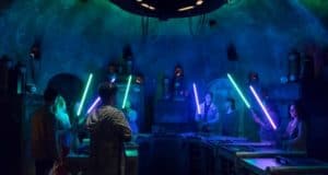 Guests wield glowing lightsabers in a futuristic Disney World setting illuminated by blue and green lights for an epic experience.
