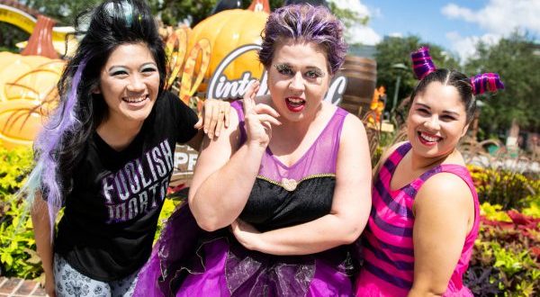 Fans in vibrant Disney Halloween outfits pose with pumpkins and retro signage, capturing the playful spirit of Disney Springs.