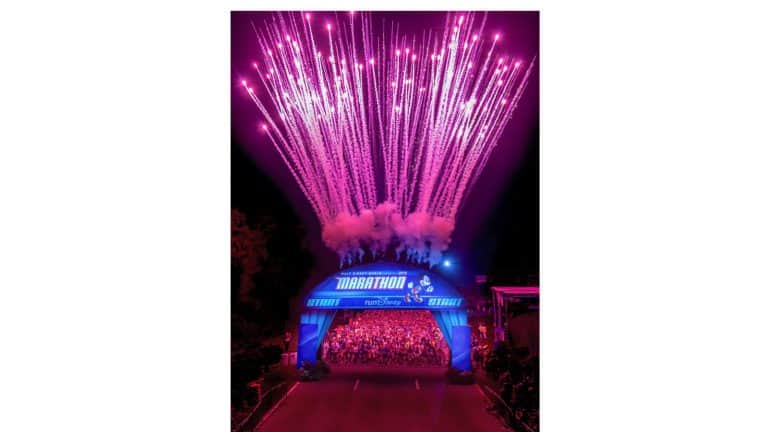 Fireworks dazzle above runners at the Walt Disney World marathon start, with a glowing blue arch setting the magical scene.