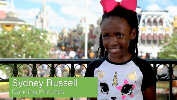 Sydney Russell, Dancing Princess, beams in a unicorn tee and pink bow outside at Walt Disney World.