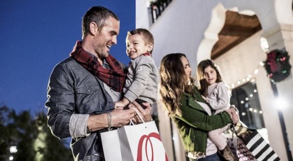 Guests with shopping bags and kids enjoy festive Black Friday magic outside a beautifully decorated Disney Springs venue at night.
