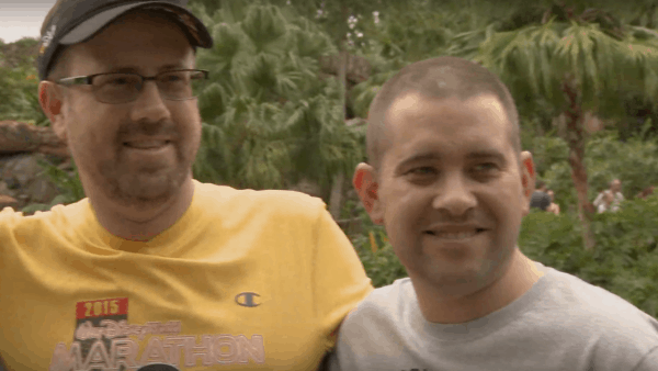 Two happy runners celebrate their Disney Wine & Dine Half Marathon finish, surrounded by magical greenery in the park.