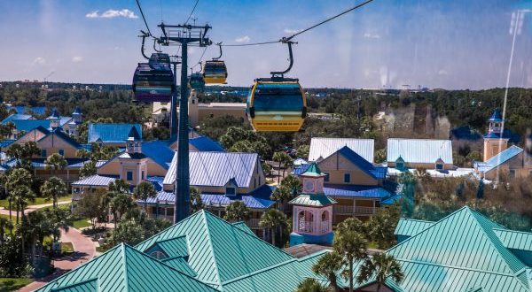 Disney Skyliner gondolas soar over Caribbean Beach Resort, gliding past palm trees on a bright day at Walt Disney World.