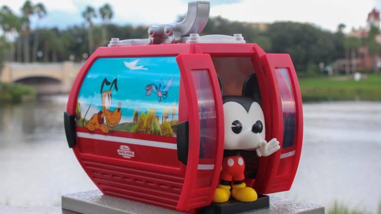 Mickey Mouse Funko Pop waves from a vibrant red Disney Skyliner gondola, decked out with playful Disney character art.