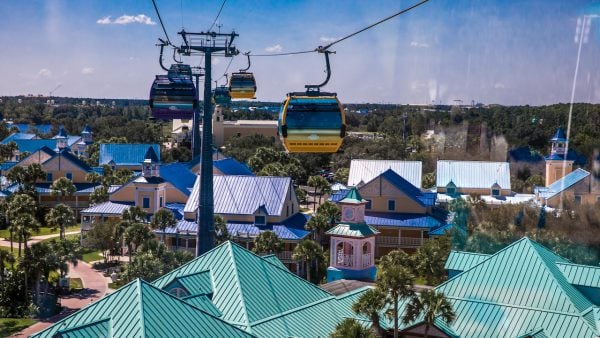 Disney Skyliner gondolas soar over Caribbean Beach Resort, gliding past palm trees on a bright day at Walt Disney World.