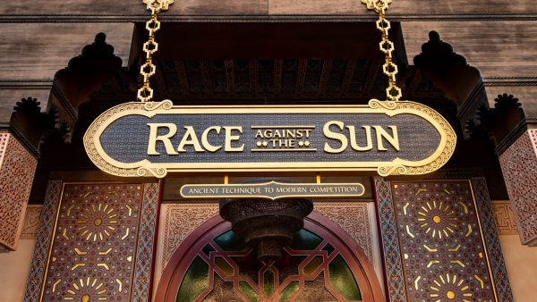 Race Against The Sun" sign with intricate patterns and gold trim stands above an entrance in Epcot’s Morocco Pavilion.