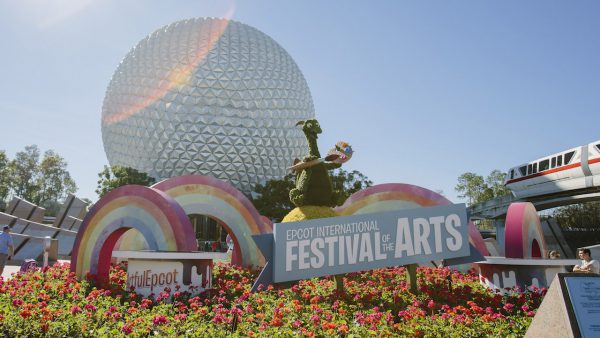 Epcot Festival of the Arts sign surrounded by vibrant flowers and rainbow arches, with Spaceship Earth as the iconic backdrop, 2020.