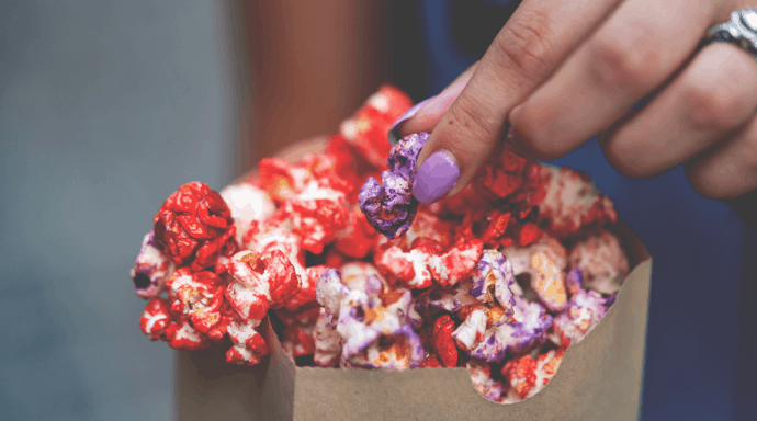 A guest with purple nails grabs vibrant Galaxy’s Edge popcorn from a paper bag, echoing the magic of Star Wars snacks.