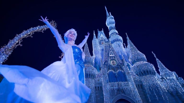 Elsa beams in front of the dazzlingly lit Cinderella Castle during Frozen Holiday Wish at Walt Disney World.