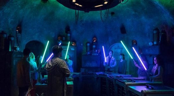 Guests wield glowing lightsabers in Star Wars: Galaxy's Edge, surrounded by blue and green sci-fi lighting for a truly immersive experience.